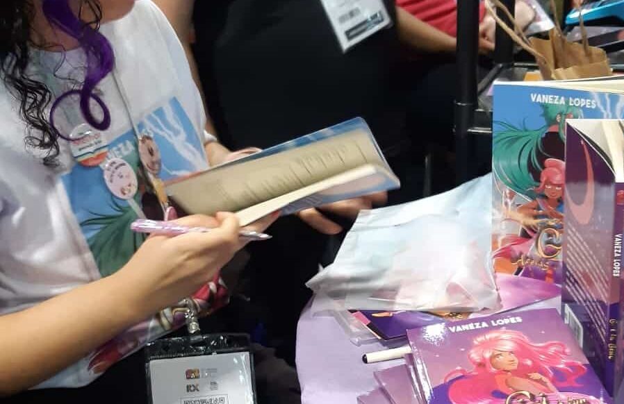 pessoa em pé segurando um livro e uma caneta em um estande de livros na bienal de são paulo